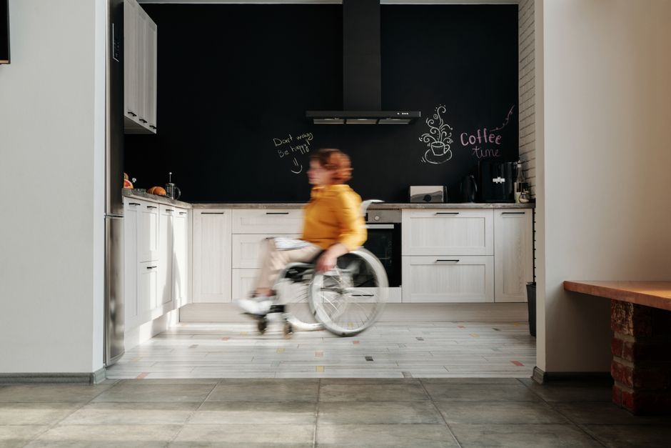 A woman in a wheelchair swiftly moves through a modern kitchen setting.